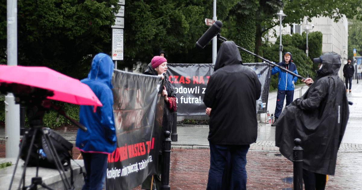 Aktywiści i dziennikarze podczas protestu stoją na deszczu.